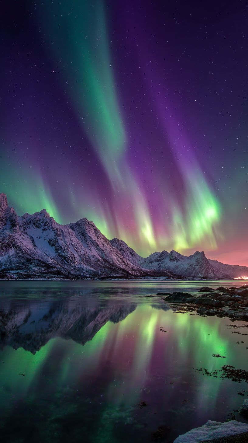 ノルウェーのフィヨルドの上空で北極光が緑と紫のリボンのように踊る