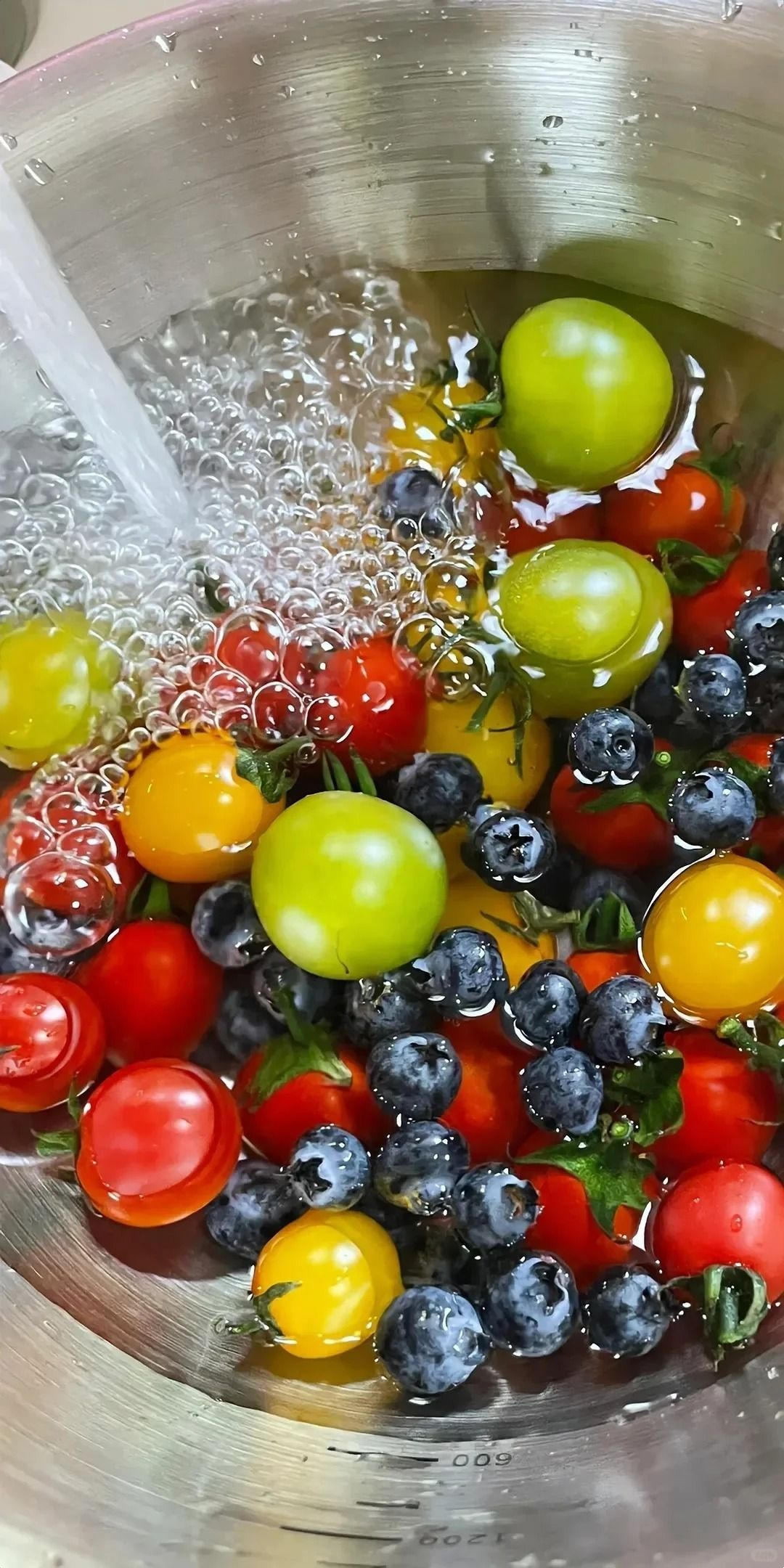 Close-up of washing colorful cherry tomatoes and blueberries in a stainless steel bowl