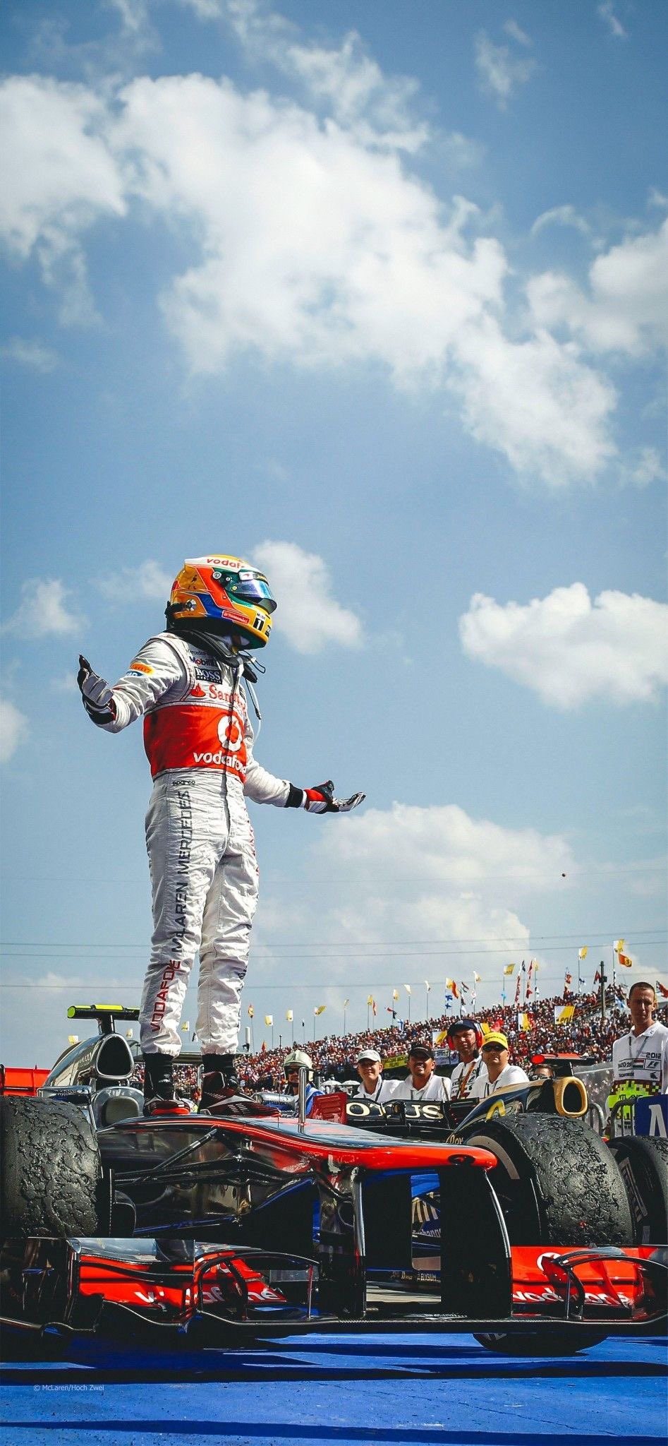 F1 드라이버가 은적색 팀복을 입고 경주차 위에 서 있다