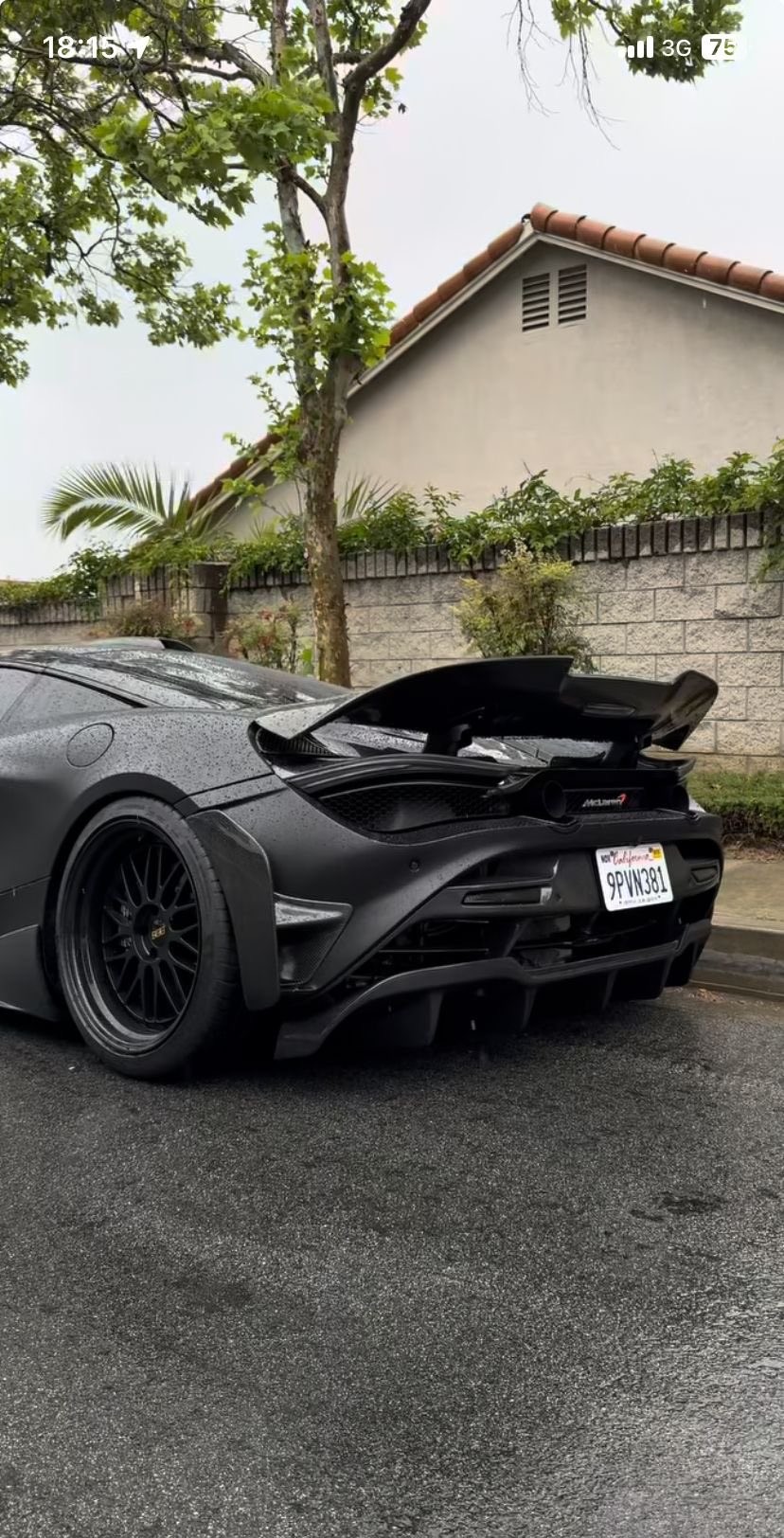 Matte black McLaren supercar parked on the rain-soaked street with drops decorating its body