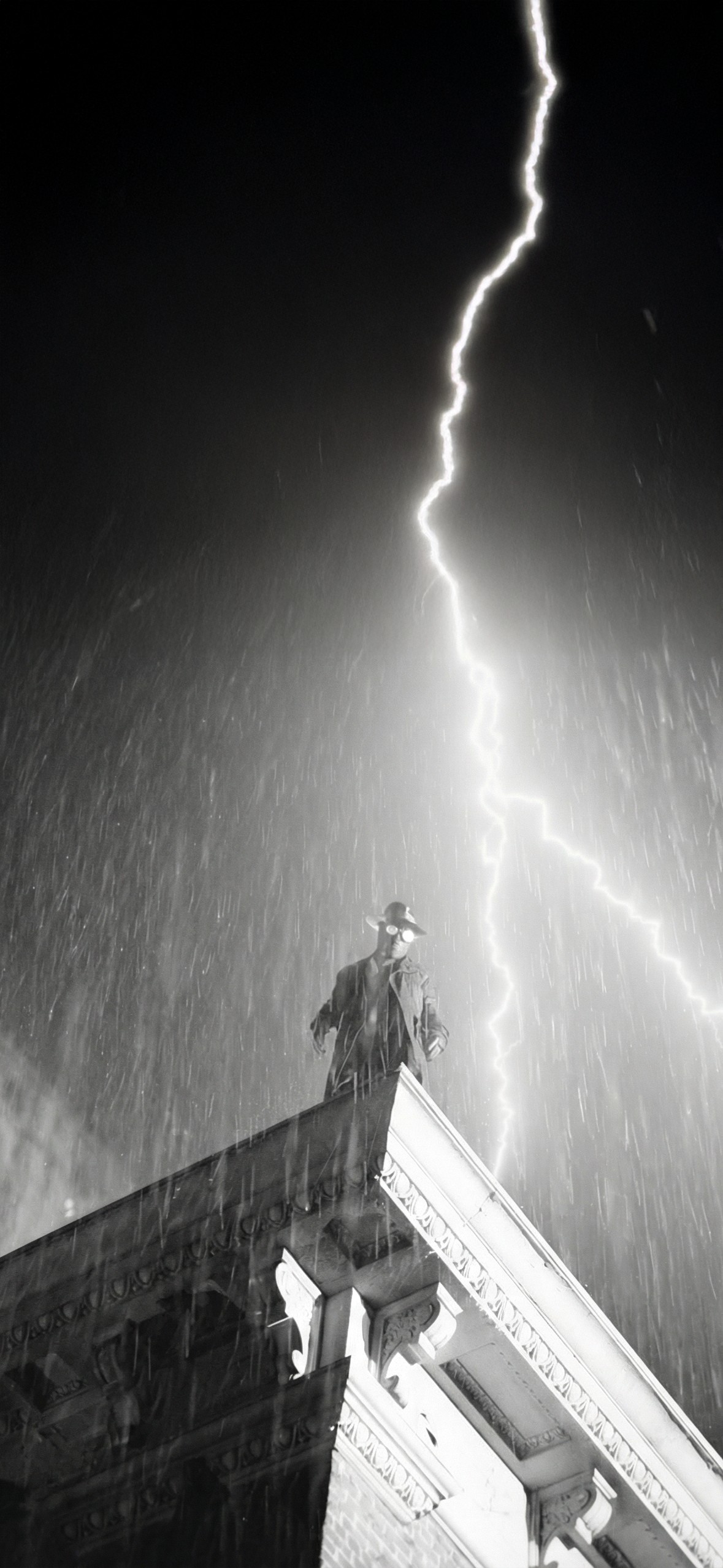 El fondo de pantalla en blanco y negro presenta a un hombre con sombrero en la cima de un antiguo edificio, creando una atmósfera misteriosa