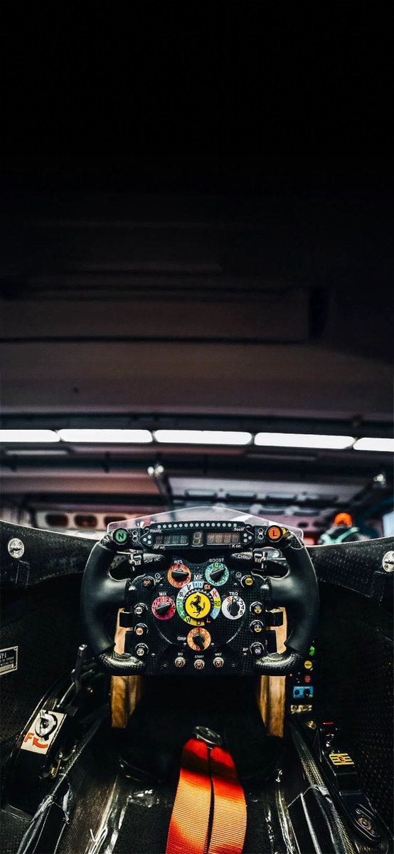 Uma foto dramática do interior de um carro focada no volante e cockpit da Ferrari F1