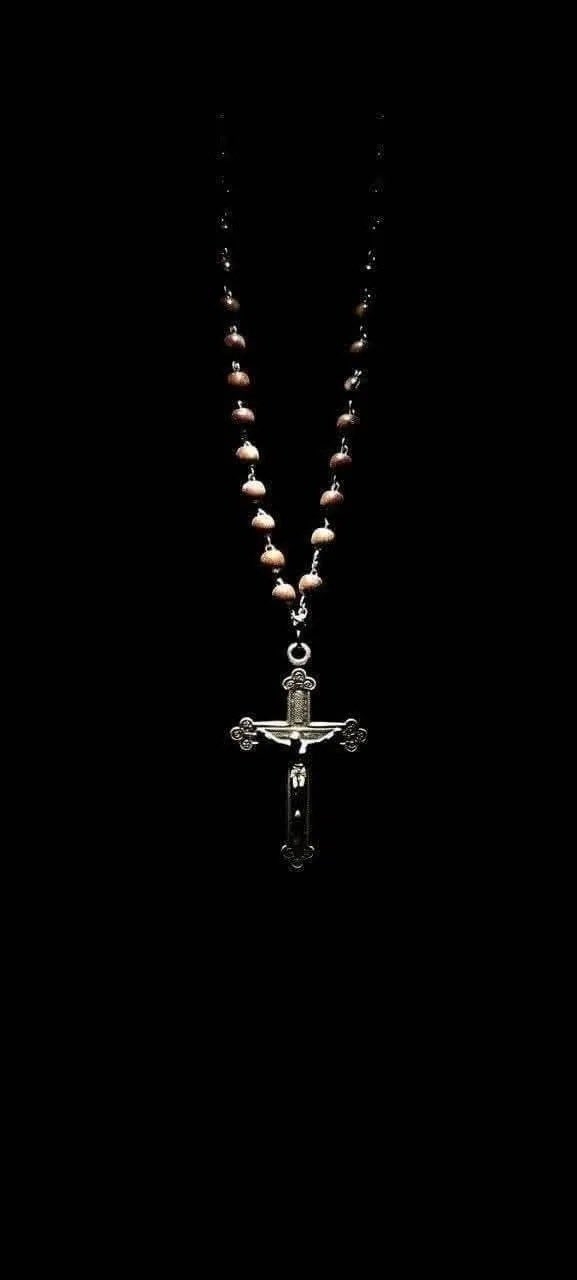 A dark background featuring a crucifix and wooden rosary beads creates a mysterious religious atmosphere