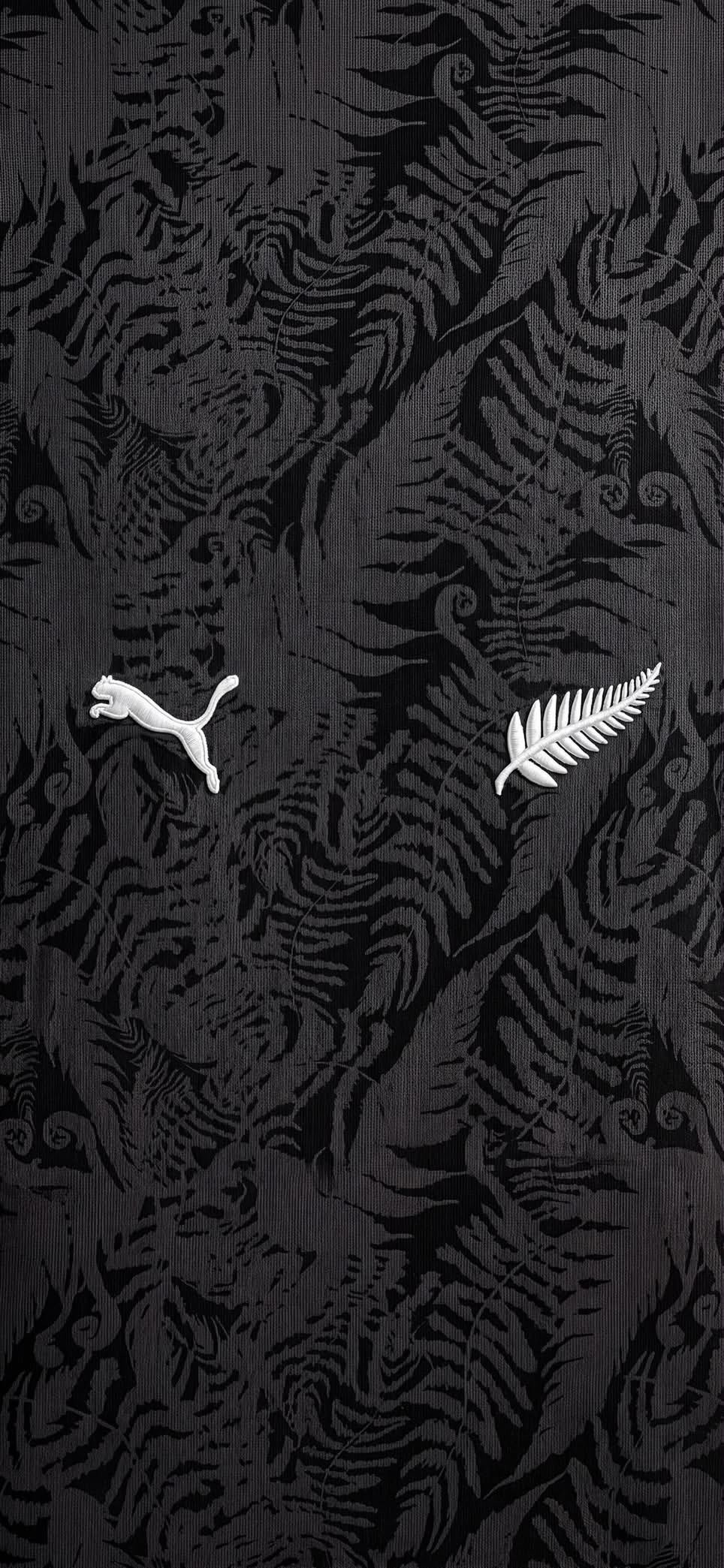 The background features a dark textured fabric with a complex fern pattern, showcasing a white Puma logo on the left and a white silver fern emblem on the right, combining New Zealand All Blacks rugby aesthetic and Puma branding