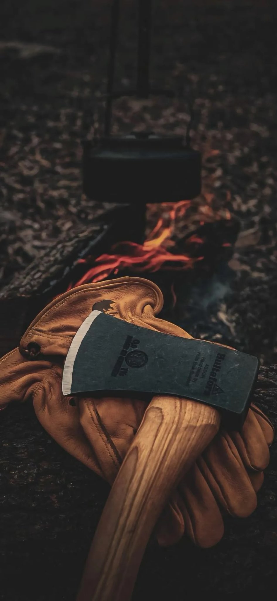A camping axe and leather gloves create an outdoor survival atmosphere with a flickering campfire