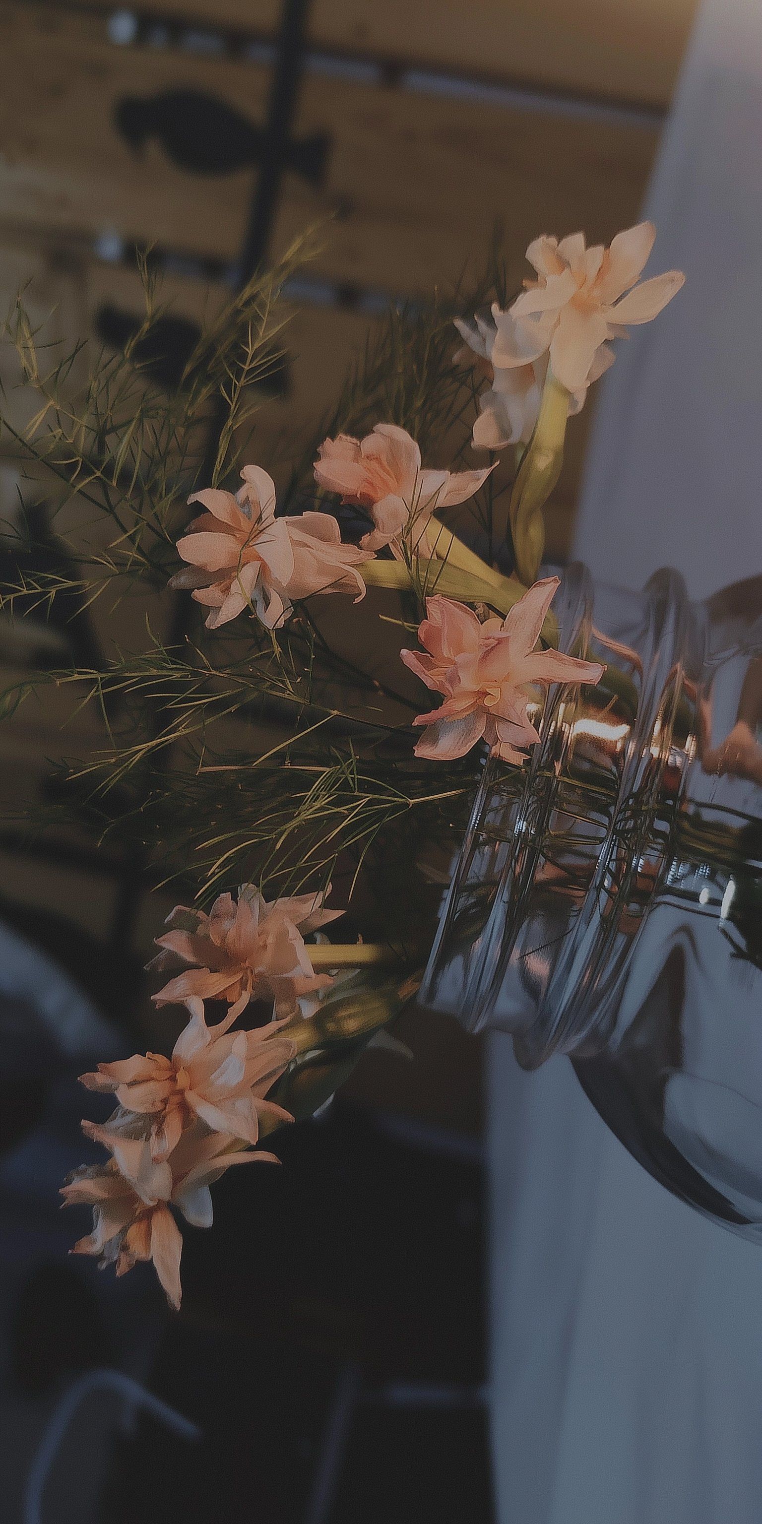 This photograph shows pale peach or salmon-colored flowers in a glass vase with delicate foliage