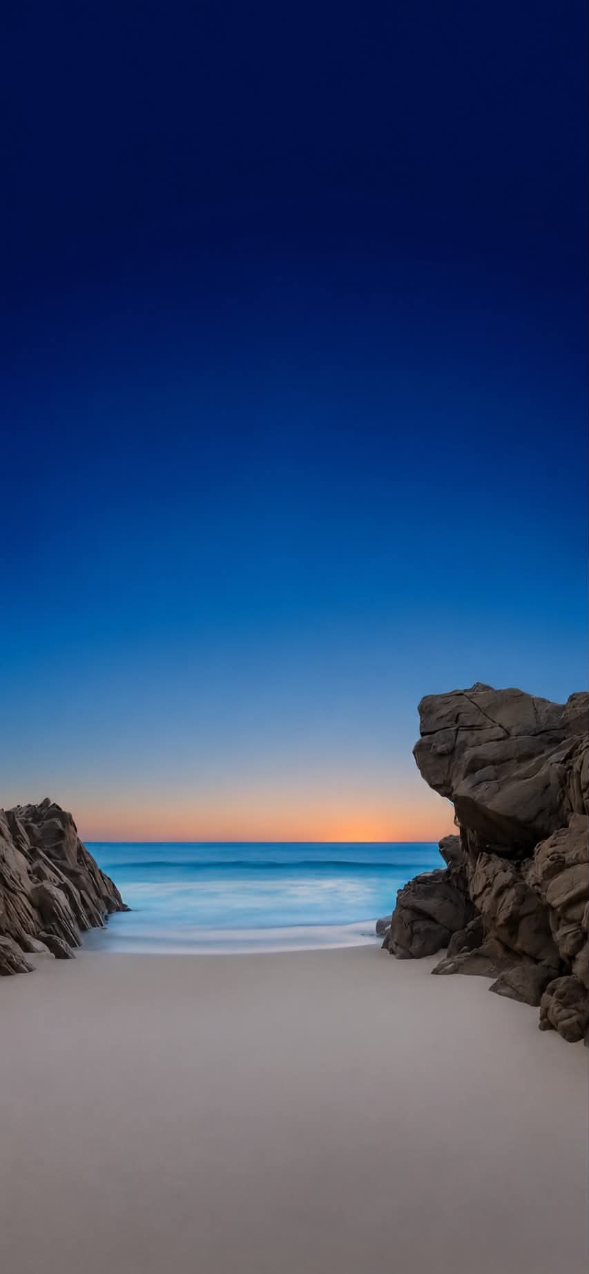 Dawn or dusk beach landscape with reefs framing calm sea and sky. Colors gradient from deep blue to orange-yellow horizon, sea in cyan-blue and sand in warm gray.