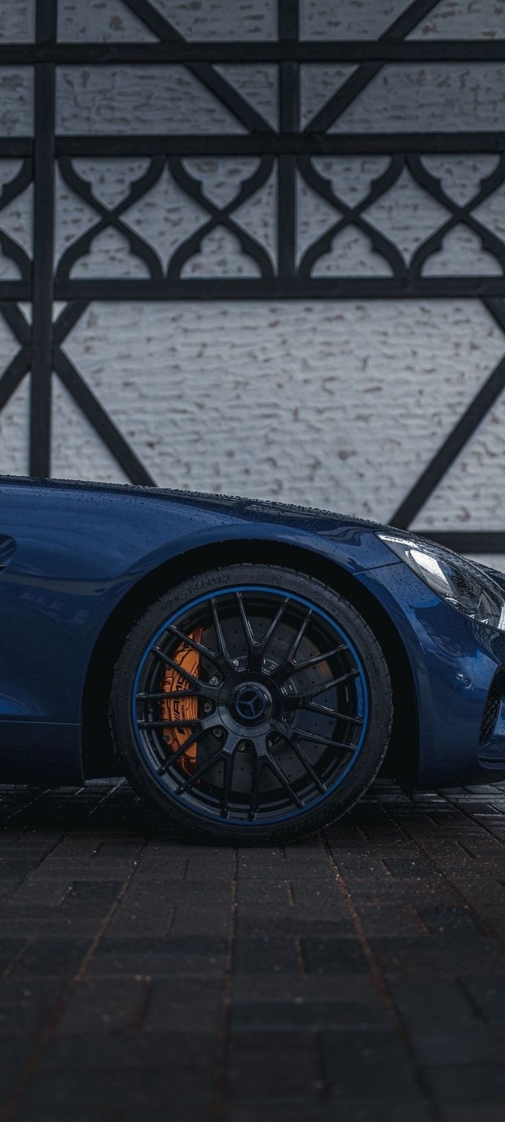 A close-up of a deep metallic blue Mercedes-AMG coupe's front wheel and fender on wet cobblestones