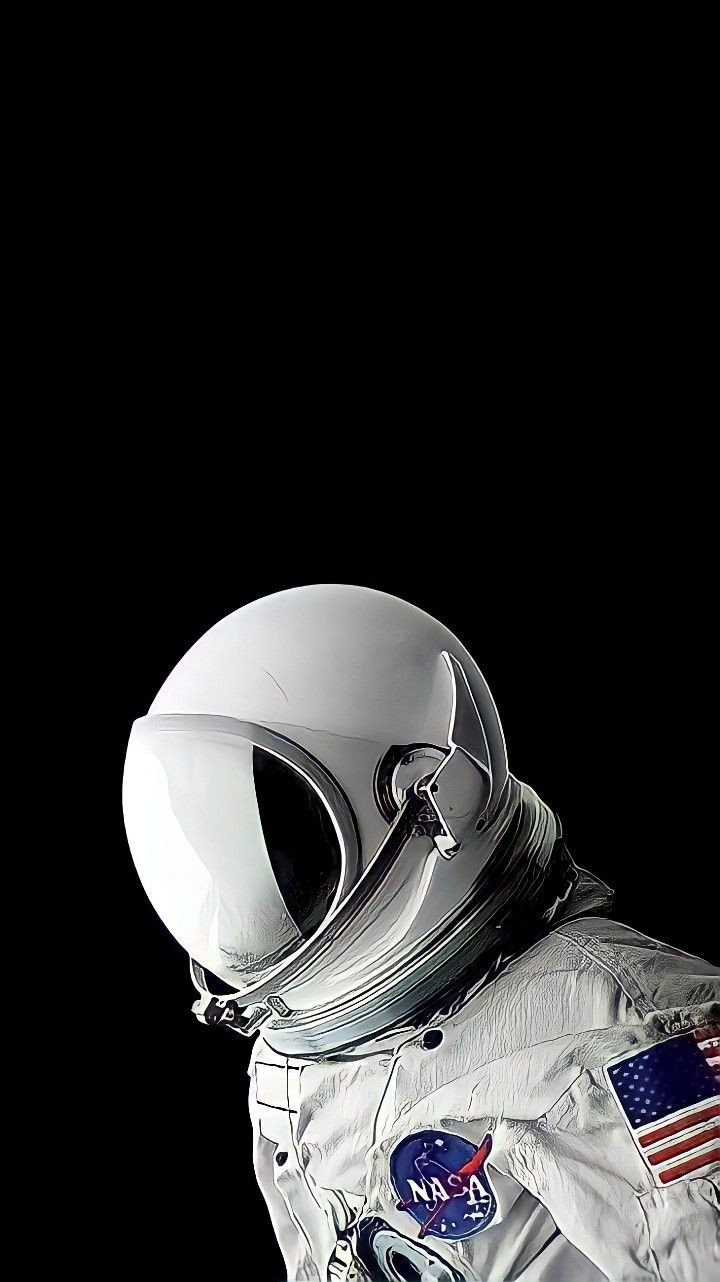 A NASA astronaut in a white spacesuit stands against a black background, showcasing quiet focus and technological precision