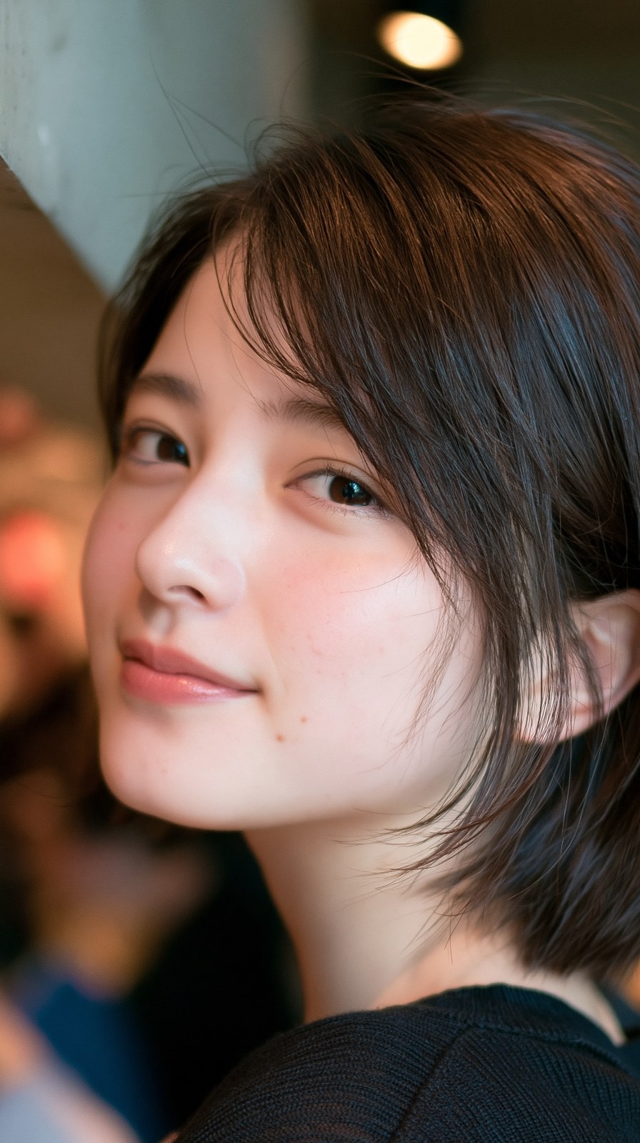 사진 속 젊은 여성은 짙은 갈색 단발을 하고 미소를 지으며 측면을 위쪽으로 바라보고 있다