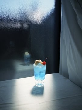 A blue drink topped with white cream and a red cherry