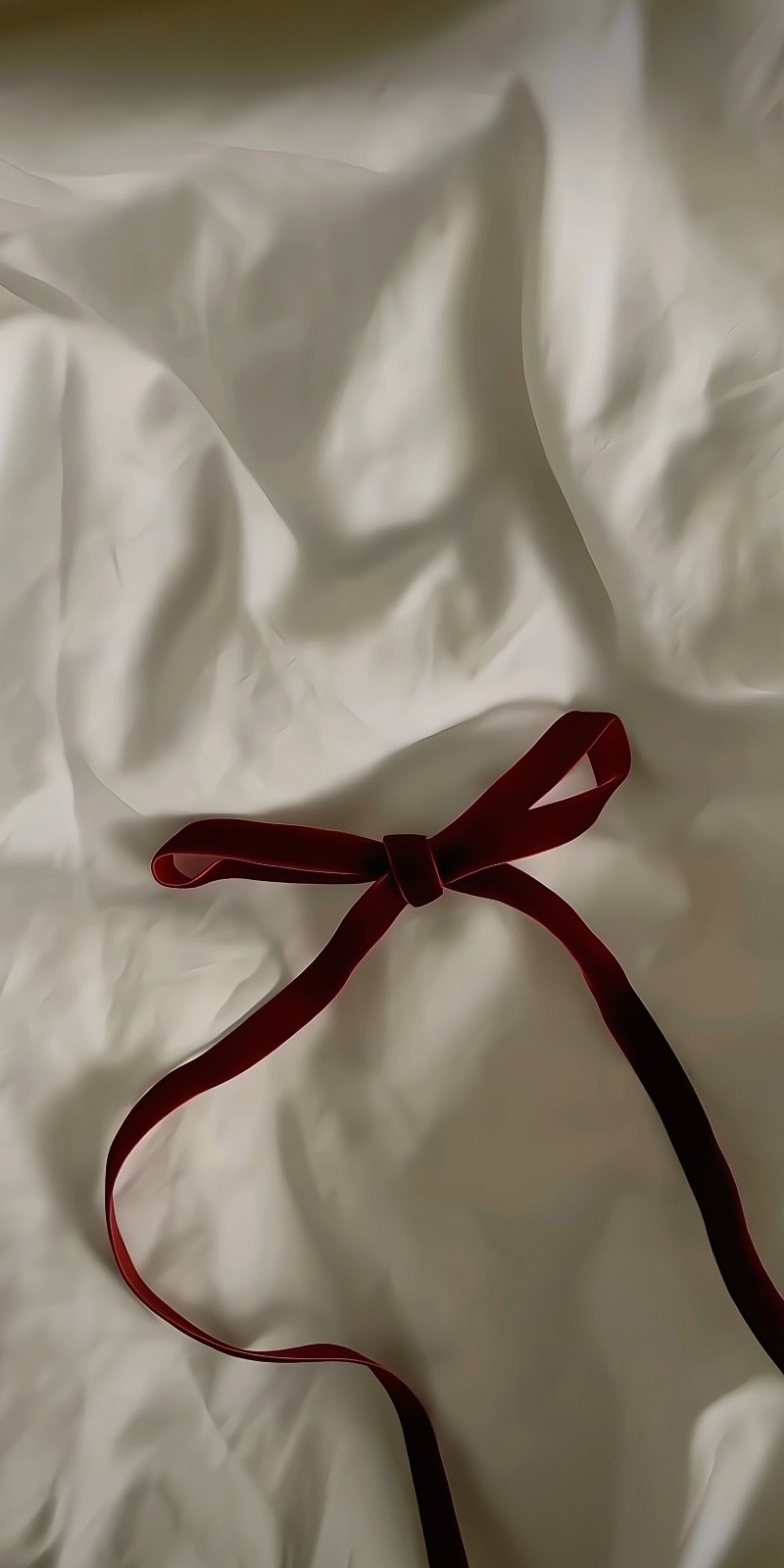 Lençóis de cor creme amassados e uma fita de veludo bordô criam uma atmosfera elegante