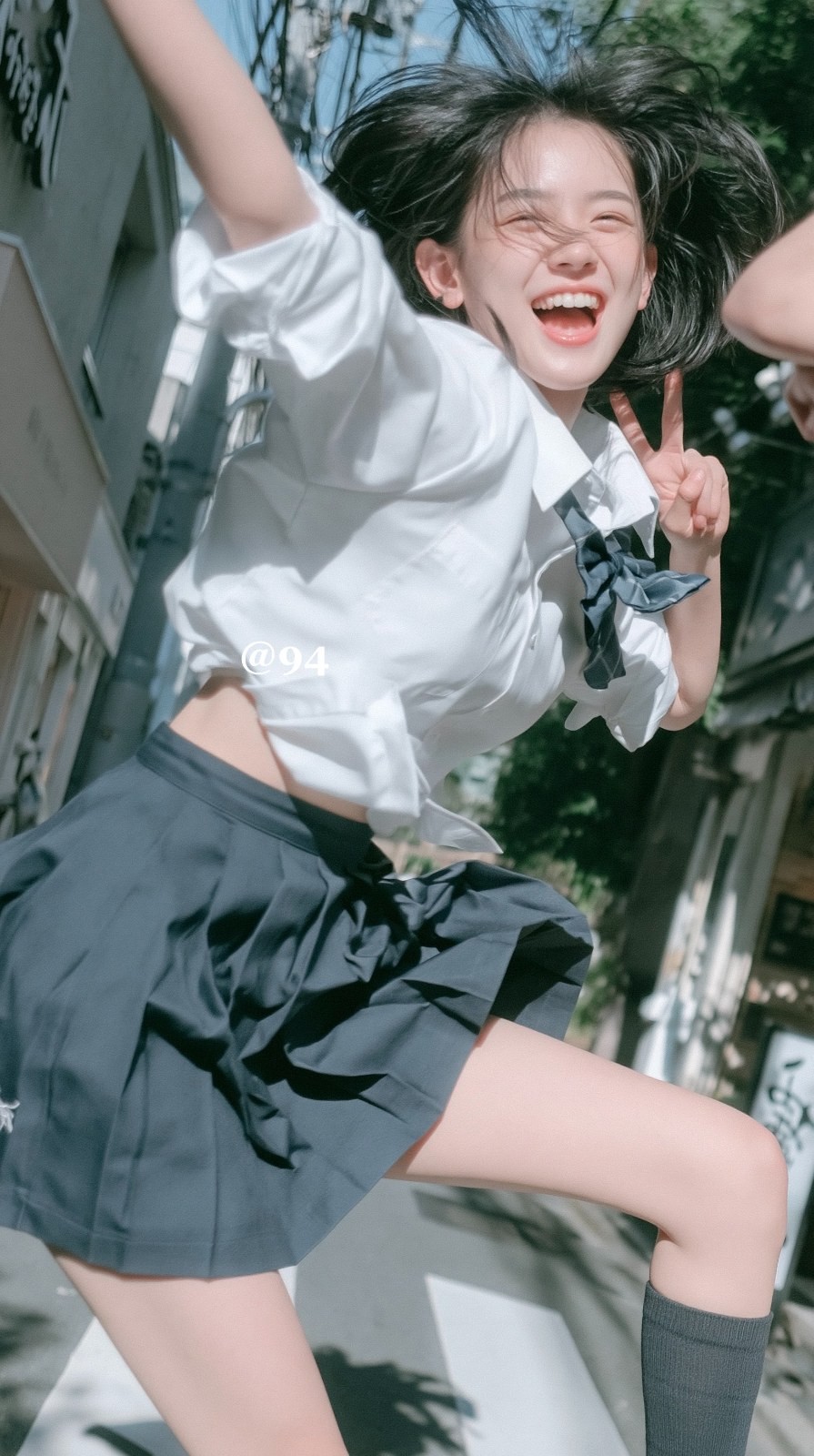 A young woman in a white short-sleeve shirt and dark pleated skirt jumps up laughing