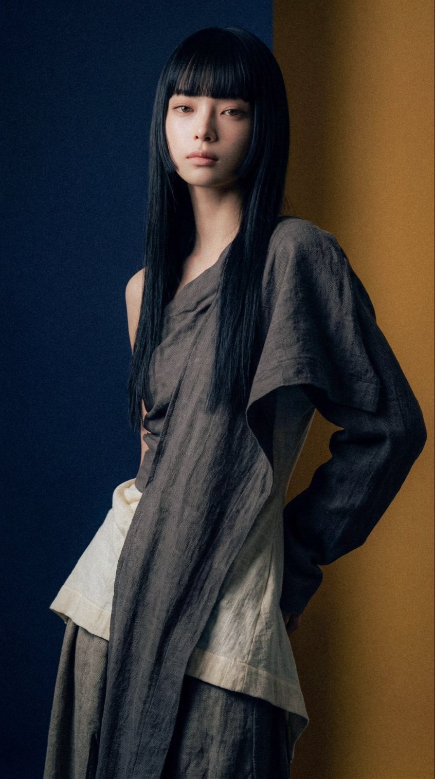 modelo femenina de pie de lado con traje plisado asimétrico gris oscuro