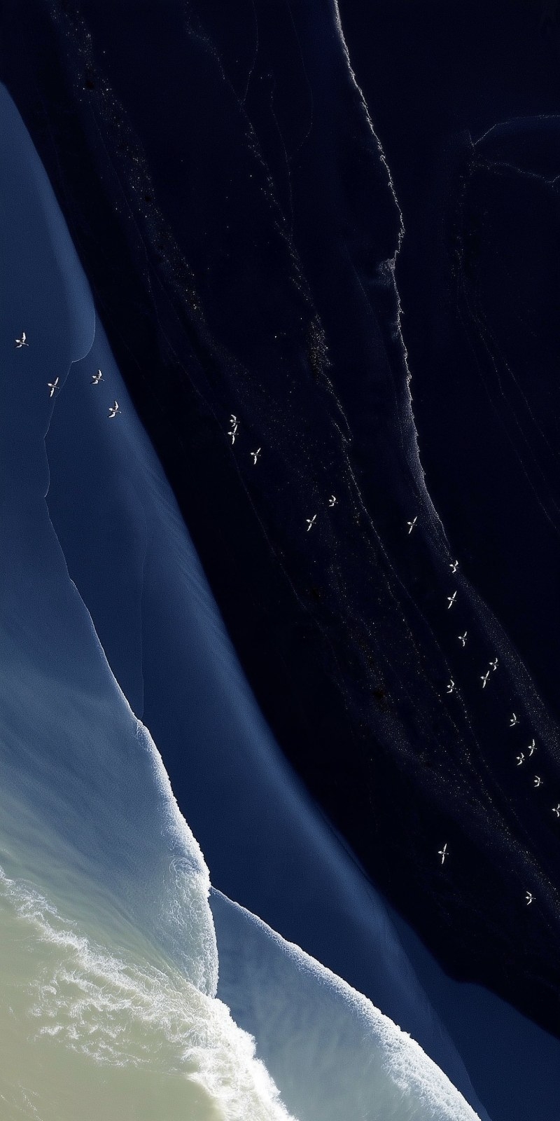 Aerial view reveals abstract geometric patterns formed by the deep blue sea and white waves