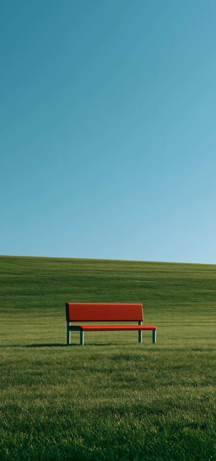 A red bench is set on a green slope under a blue sky