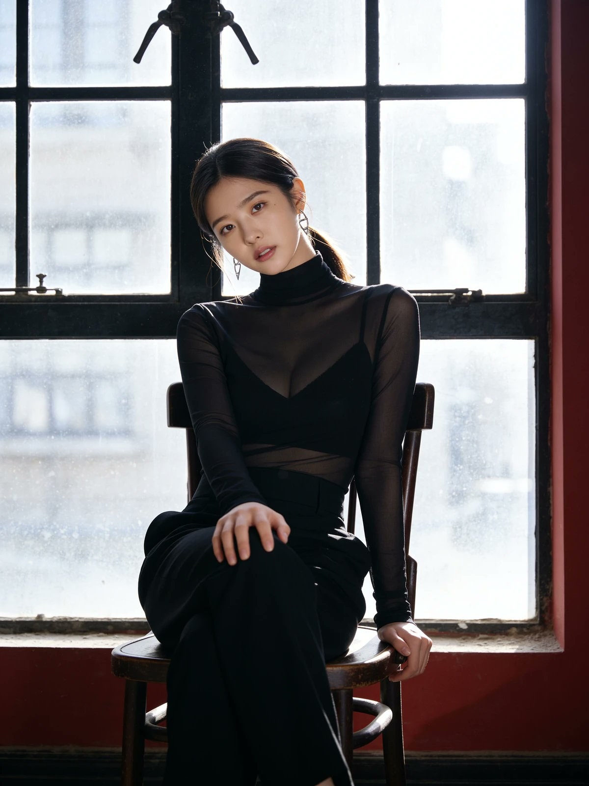 A young woman is sitting on a chair wearing a black turtleneck sheer top and pants