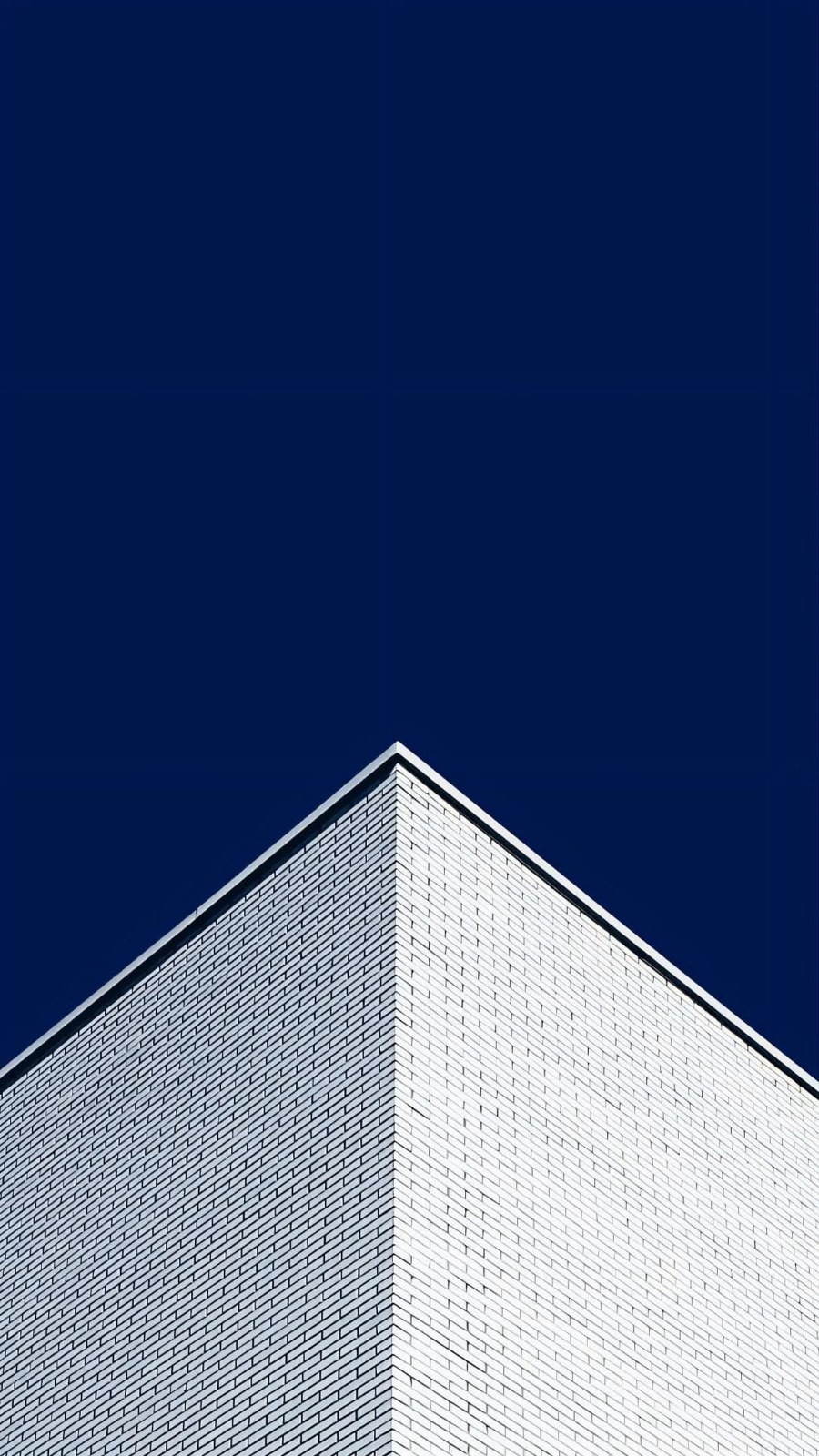 Modern building top edges under deep blue sky geometric outline low angle white brick walls pale tiles converge