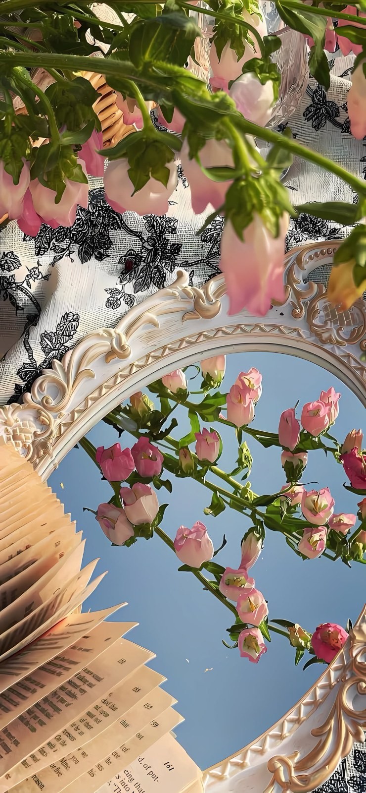Miroir ovale sculpté reflétant ciel bleu et branches fleuries avec feuilles vertes, fleurs roses et un vieux livre, vintage et frais