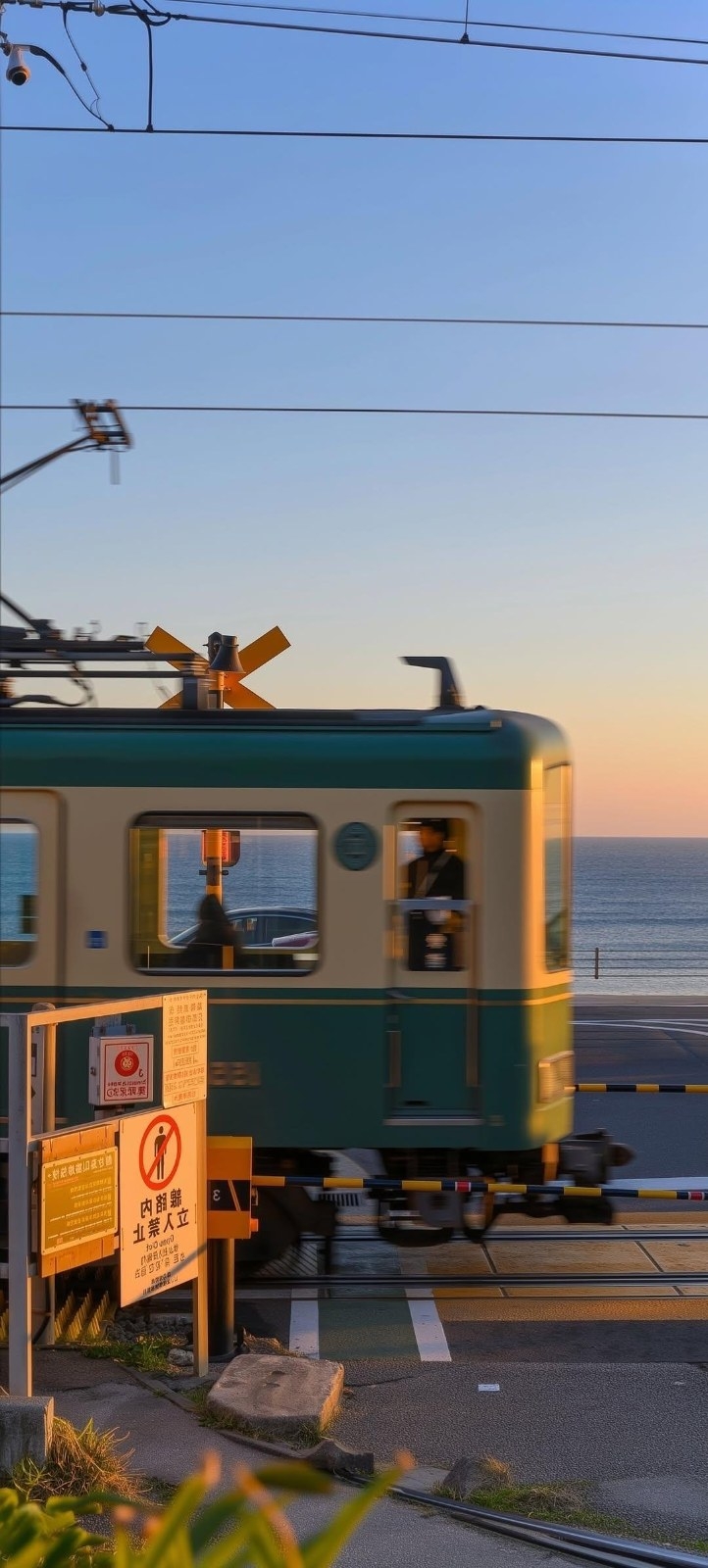 At dusk, a green and white tram passes through a coastal railroad crossing, bathed in warm evening light