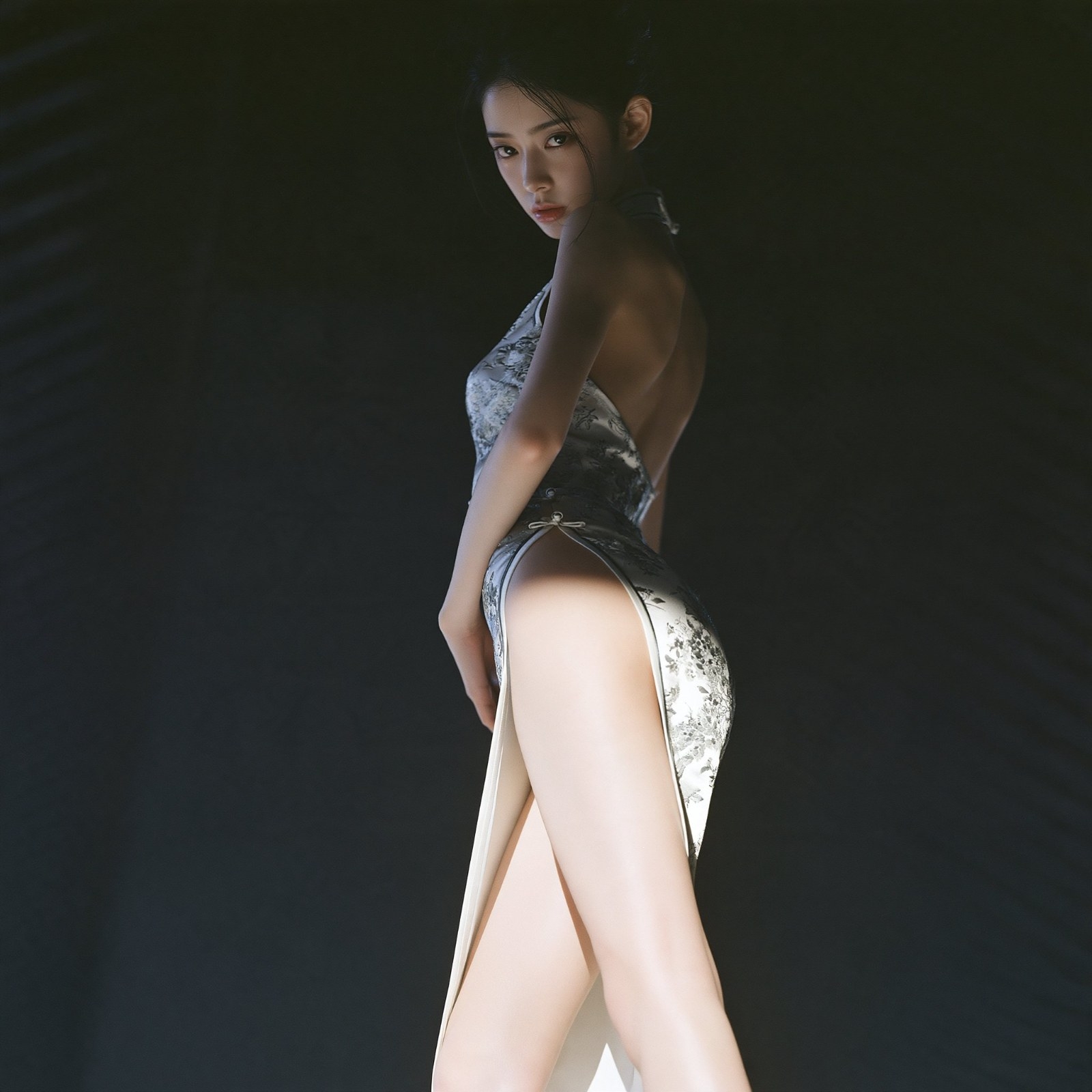 Frau im silbergrauen Jacquard-Modern-Qipao zeigt Rücken- und Beinlinien im Seitenprofil