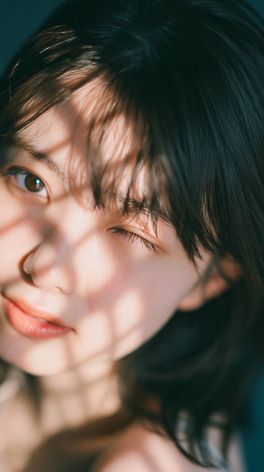 Close-up do rosto de uma jovem, jogo de luz e sombra, piscadela e sorriso, clima de filme japonês